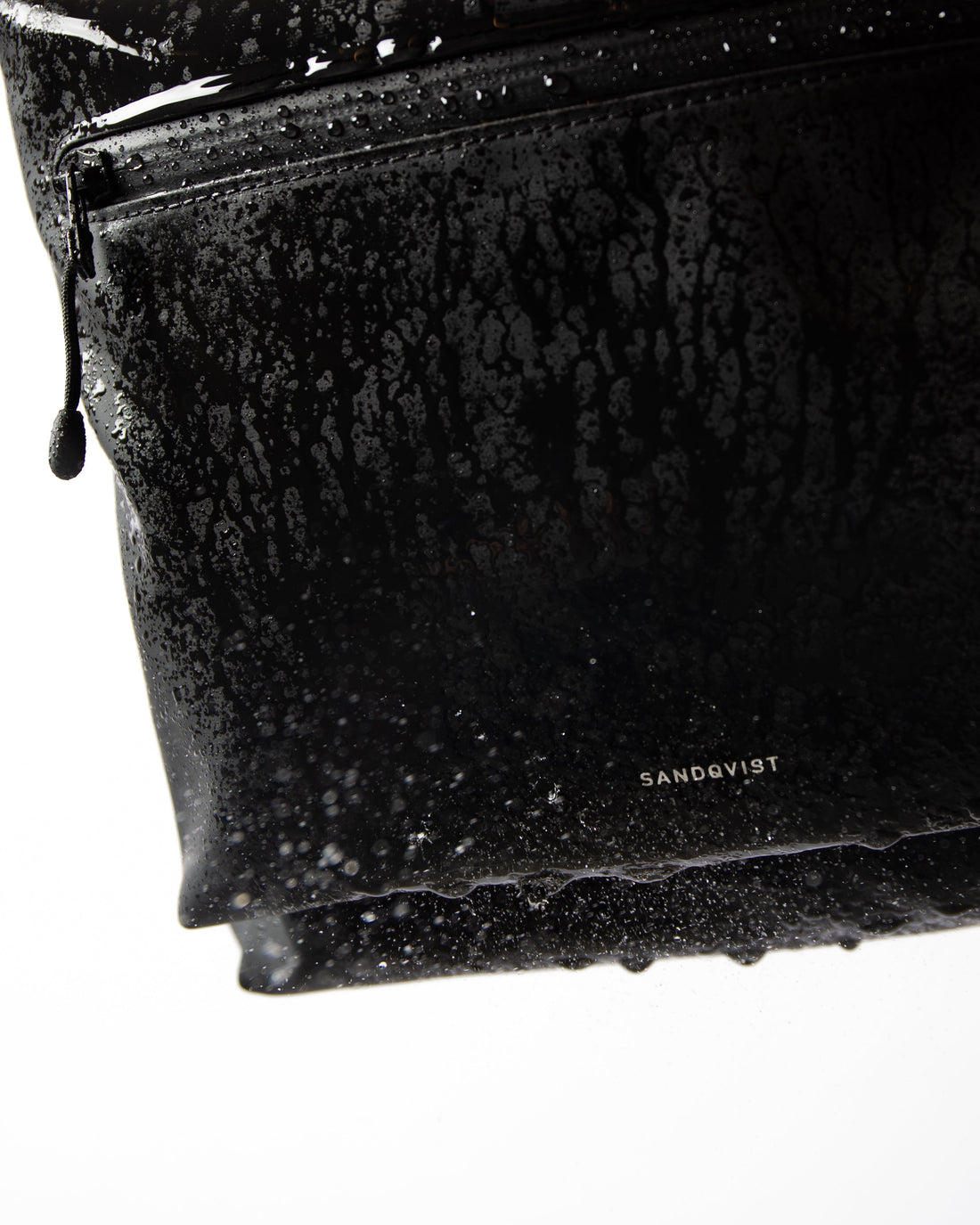 Sandqvist STREAM Rolltop Backpack L noir — détail du revêtement et de la poche zippée avec des gouttes d’eau.