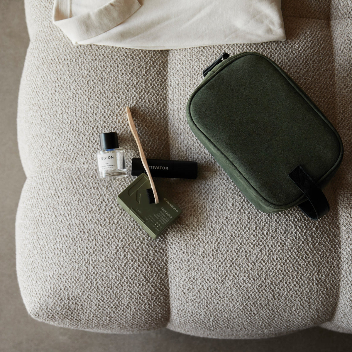 Trousse de toilette kaki posée sur un fauteuil avec des accessoires