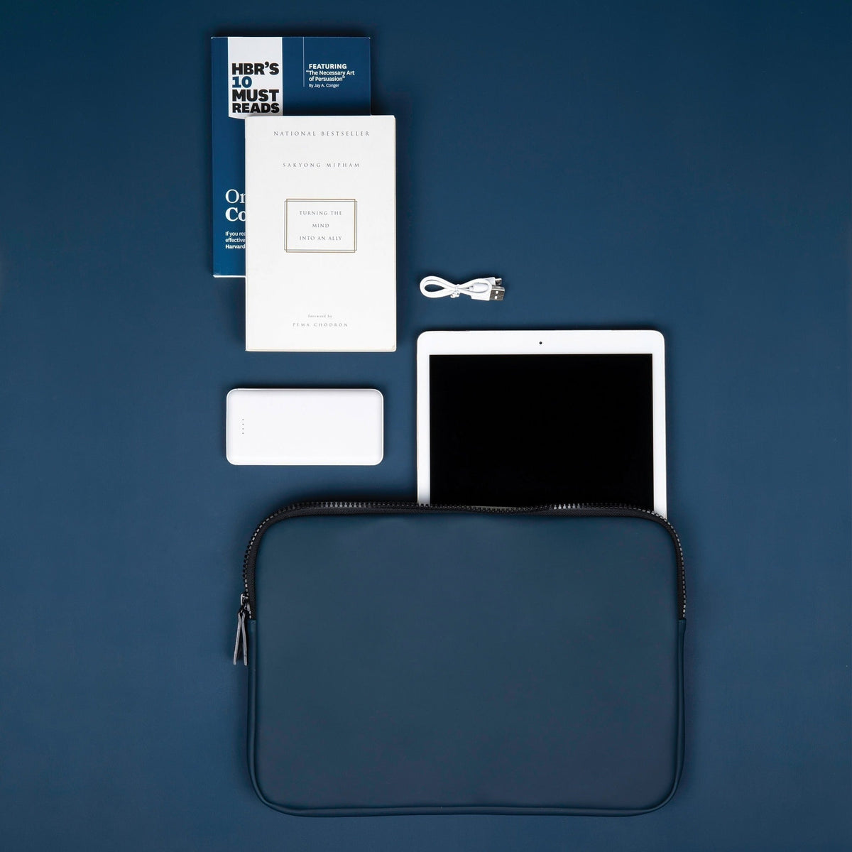 Pochette d’ordinateur bleu marine posée à plat avec tablette, carnet et accessoires