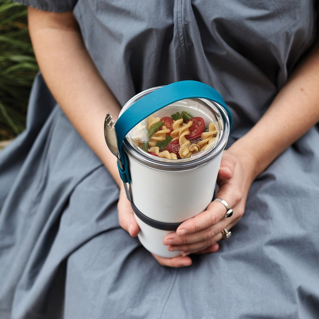 Personne tenant un lunchpot Black+Blum blanc et turquoise ouvert avec un repas