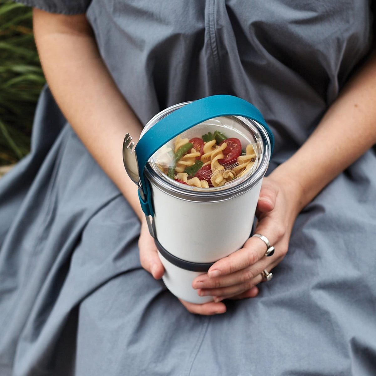 Personne tenant un lunchpot Black+Blum blanc et turquoise ouvert avec un repas